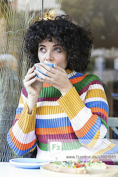 Frau mit lockigem Haar trinkt Kaffee  während sie im Restaurant sitzt