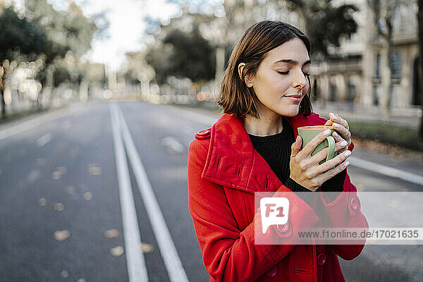 Junge Frau mit geschlossenen Augen riecht an Kaffee  während sie auf der Straße steht