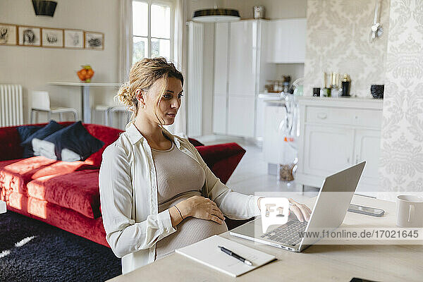Schwangere Geschäftsfrau arbeitet am Laptop am Schreibtisch zu Hause
