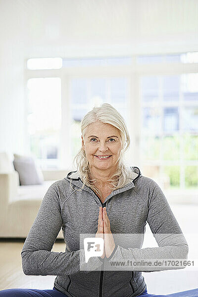 Lächelnde ältere Frau mit verschränkten Händen beim Sport zu Hause