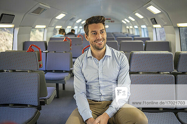 Lächelnder Geschäftsmann  der wegschaut  während er im Zug sitzt