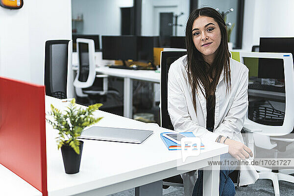 Lächelnde Geschäftsfrau mit Laptop und Smartphone auf dem Schreibtisch sitzend
