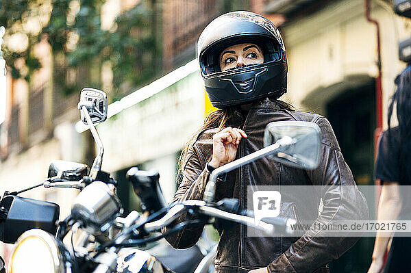Biker woman in helmet wearing leather jacket while looking away in city