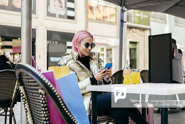Frau lächelt  während sie in einem Straßencafé sitzt und ein Mobiltelefon benutzt