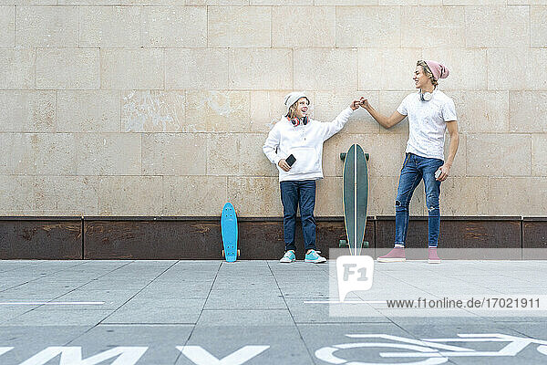 Freunde geben sich einen Faustschlag  während sie auf dem Gehweg neben Skateboards stehen