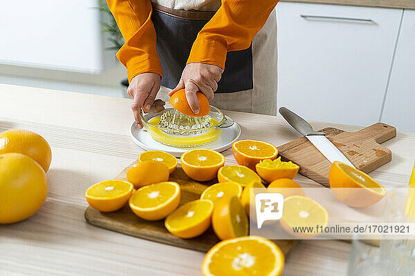 Frau  die eine Orange in der Saftpresse auspresst  während sie in der Küche zu Hause Saft zubereitet