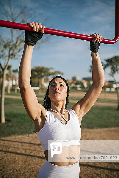Female athlete with arms raised holding red pole in public park on sunny day