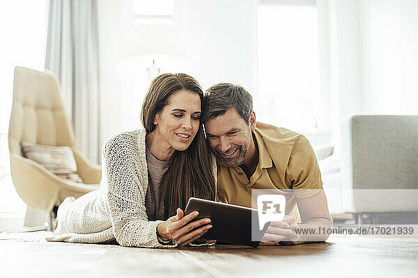 Lächelndes reifes Paar  das gemeinsam ein digitales Tablet benutzt  während es auf der Vorderseite einer Wohnung liegt