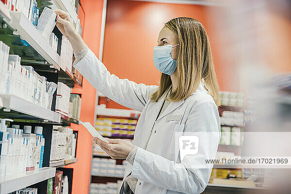Pharmacist wearing protective face mask while working in chemist store