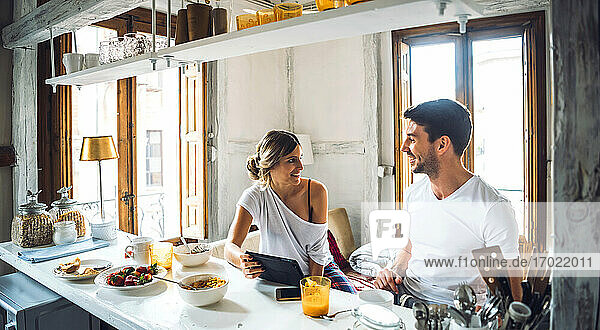 Glückliches junges Paar mit Tablette beim Frühstück zu Hause