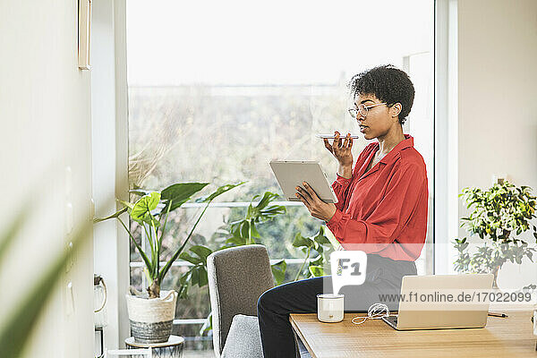 Woman using smart phone and digital tablet at table with laptop at home