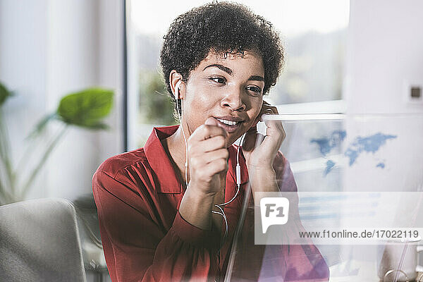 Lächelnde Frau mit Ohrstöpseln  die auf ein transparentes Display zu Hause schaut