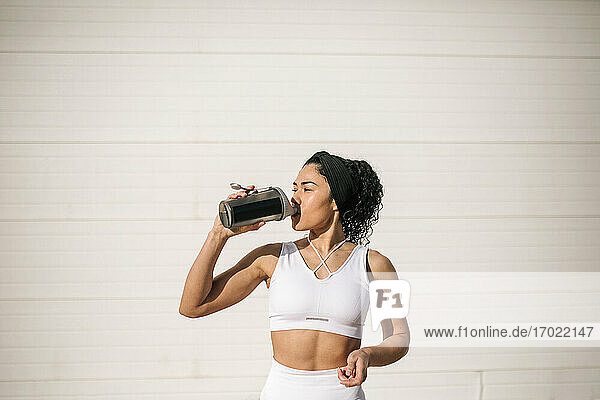 Sportlerin trinkt Wasser an der Wand an einem sonnigen Tag