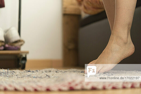 Mittlere erwachsene Frau  die ihre nackten Füße auf einen handgefertigten Teppich zu Hause stellt