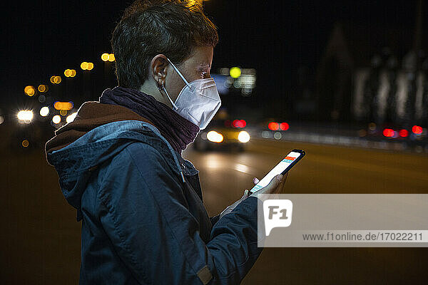 Frau mit Schutzmaske  die in der Stadt stehend ein Mobiltelefon benutzt