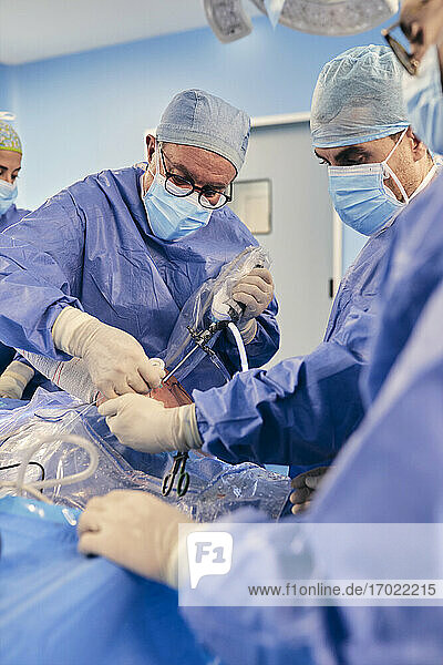Älterer Arzt  der eine arthroskopische Operation an der Schulter mit einem Kollegen durchführt  während er im Operationssaal bei COVID-19 steht