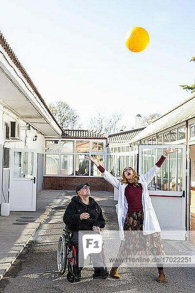 Fröhliche Krankenschwester und behinderter Mann spielen mit Ball gegen den Himmel im Rehabilitationszentrum