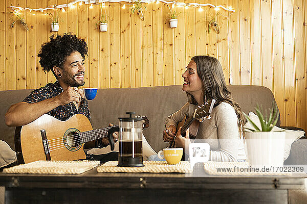 Freund trinkt Tee und sitzt bei seiner Freundin  die zu Hause Gitarre spielt
