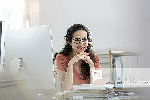 Lächelnde Geschäftsfrau mit Hand am Kinn im Büro sitzend