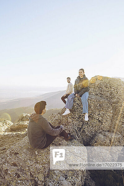 Freunde unterhalten sich auf dem Gipfel eines Berges bei klarem Himmel an einem sonnigen Tag