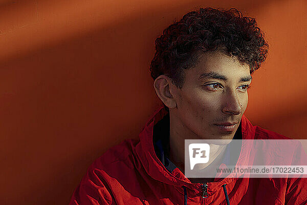 Nahaufnahme eines nachdenklichen jungen Mannes  der an einer orangefarbenen Metallwand sitzt