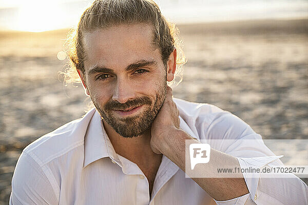 Smiling handsome young man relaxing at beach during sunset