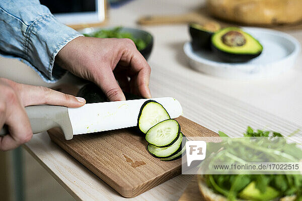 Hands of woman slicing cucumber on cutting board
