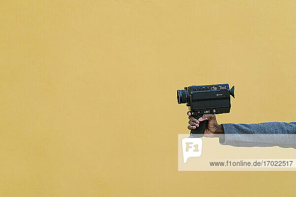 Mann hält 1980er Kamera gegen gelbe Wand