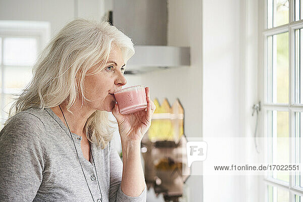 Ältere Frau im Ruhestand trinkt Erdbeer-Smoothie in der Küche zu Hause