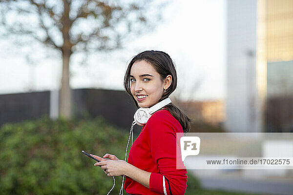 Junge Frau mit Kopfhörern und Smartphone im Park