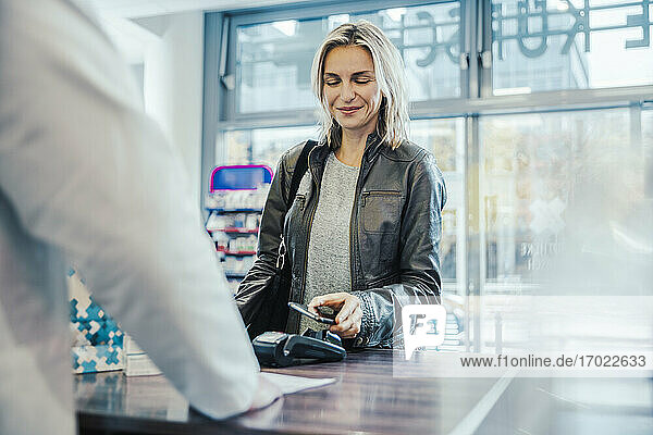 Lächelnder Kunde beim Bezahlen mit dem Handy an der Kasse eines Drogeriemarktes