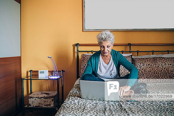 Fotograf auf dem Bett sitzend mit Laptop
