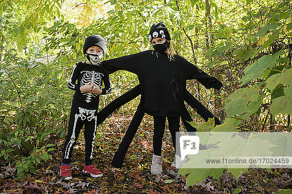 Mädchen (8-9) und Junge (6-7) tragen Halloween-Kostüme im Wald