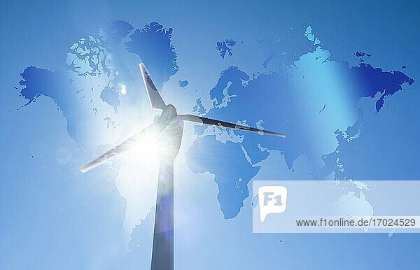 Windkraftanlage gegen blauen Himmel und Sonne mit Weltkarte im Hintergrund