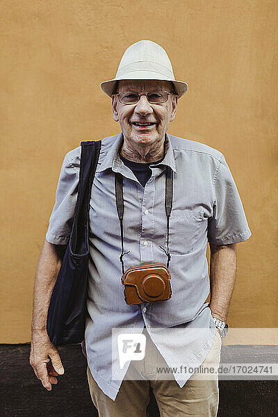 Lächelnder älterer Mann mit Hand in der Tasche an der Wand