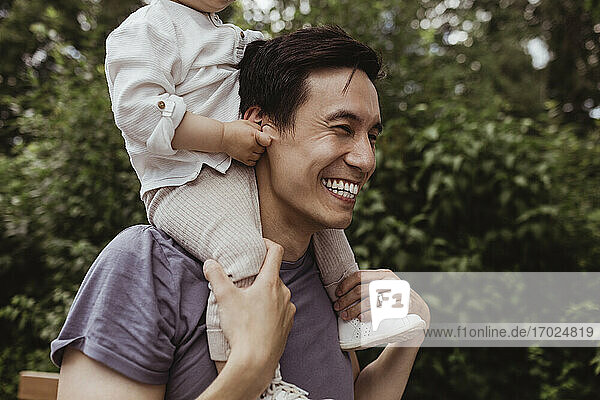 Lächelnder Vater trägt männliches Kleinkind auf der Schulter im Park