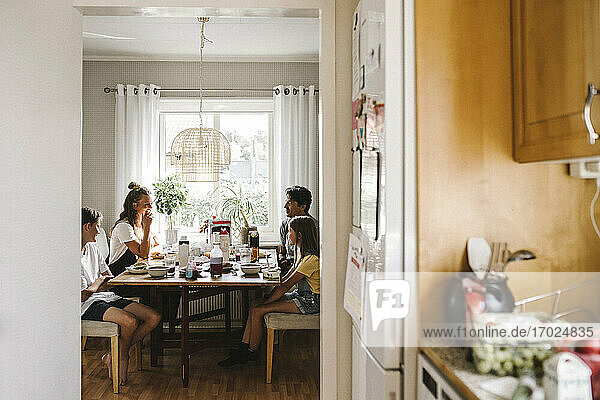 Happy family eating breakfast seen through doorway of kitchen at home