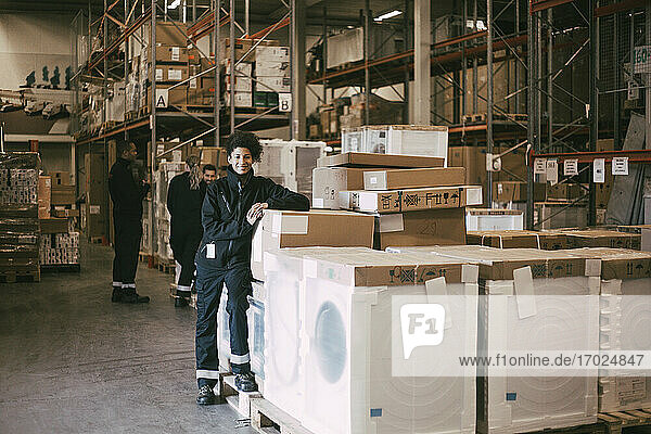 Lächelnde Unternehmerin lehnt sich an Boxcontainer im Auslieferungslager