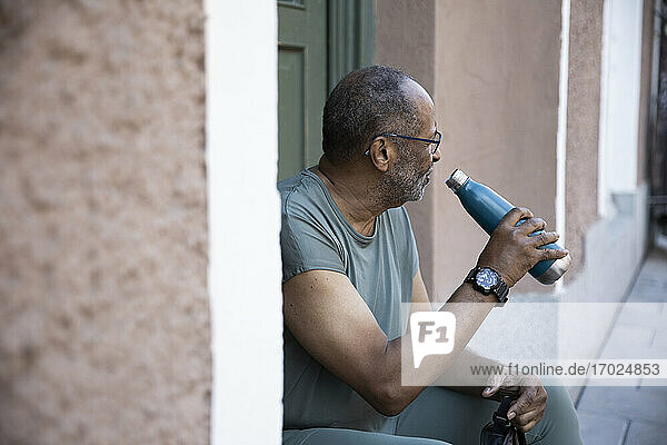 Durstiger älterer Mann mit Flasche vor der Haustür