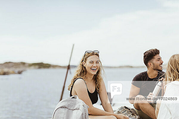 Young friends laughing while enjoying picnic against sea and sky