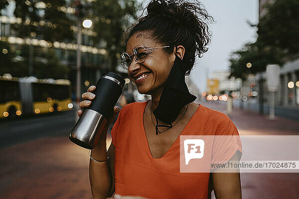 Happy female entrepreneur with insulated drink container in city during pandemic