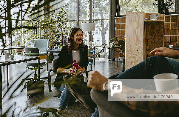 Lächelnde Unternehmerin diskutiert mit männlichem Kollegen während der Kaffeepause im Coworking-Büro