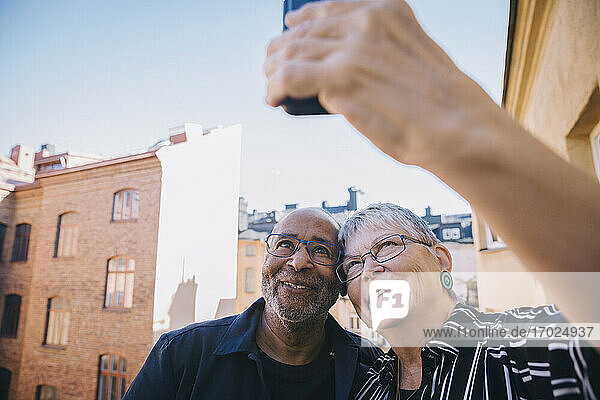 Lächelndes Paar nimmt Selfie durch Smartphone gegen Himmel in Balkon