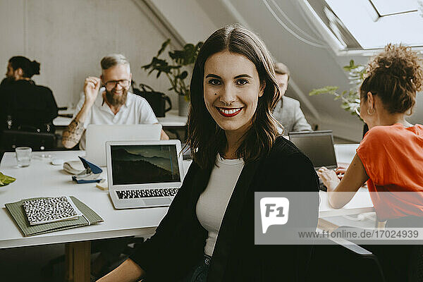 Lächelnde junge Geschäftsfrau sitzt mit Kollegen im Coworking-Büro