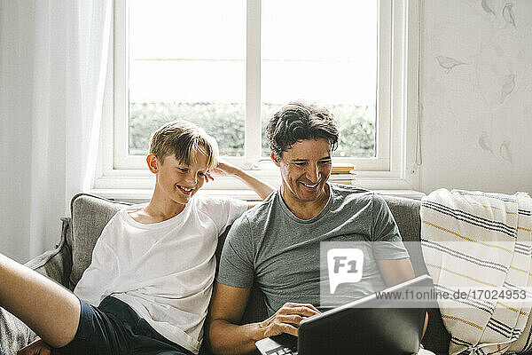 Glücklicher Vater mit Laptop  während er bei seinem Sohn im Wohnzimmer sitzt