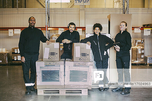 Portrait of smiling manual workers standing with box containers at logistics warehouse