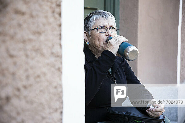 Durstige Frau trinkt Wasser aus einer Flasche am Eingang