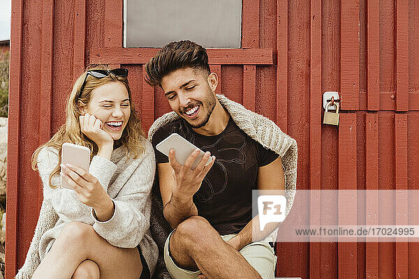Freunde lachen bei der Verwendung von Mobiltelefon gegen Hütte