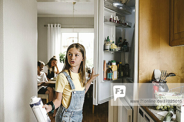 Kaukasisches Mädchen mit Saftpackung stehend am Kühlschrank