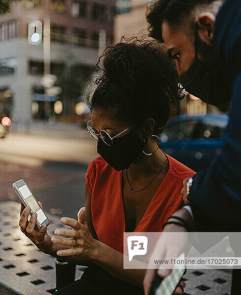 Weibliche Unternehmerin bei der Nutzung eines Smartphones mit einem männlichen Kollegen in einer Stadt während einer Pandemie